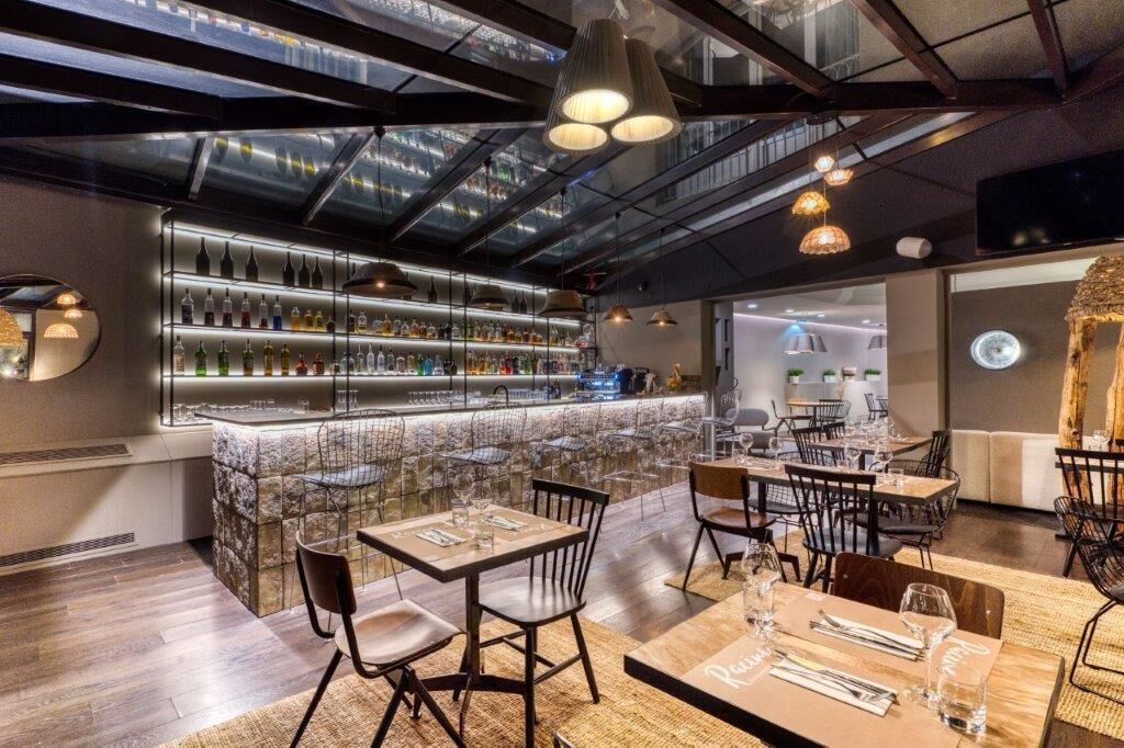 A modern bar area with a glass ceiling, wooden tables, and chairs.