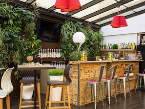 Zona de bar con taburetes de madera, una barra con botellas y una gran pantalla de televisión.