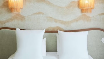 Et hotelværelse med en seng, to puder, en sengegavl og to vægmonterede lamper.