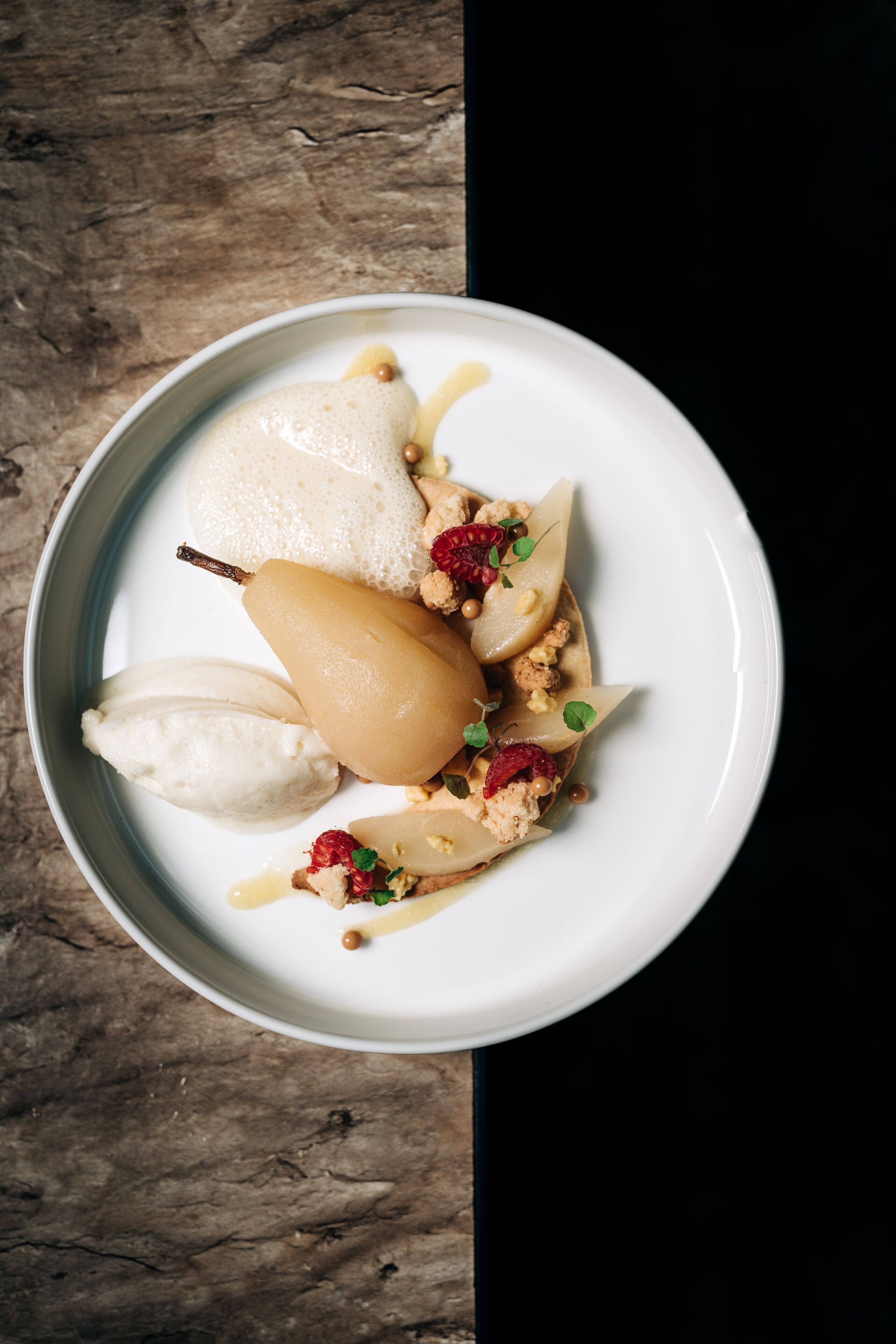 Une assiette blanche contenant un dessert composé de poires, une boule de glace et des éléments de décoration.