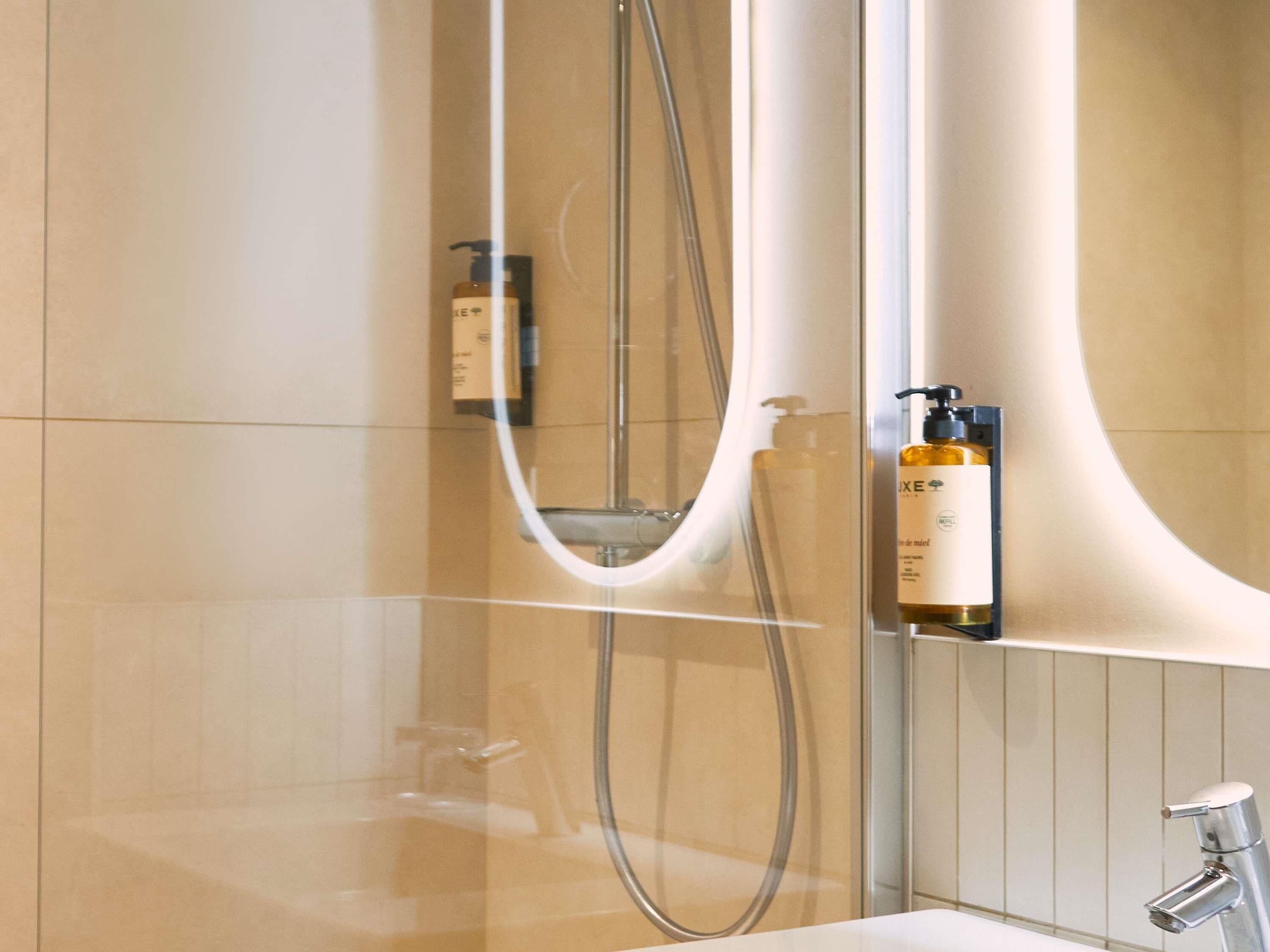 Une salle de bain moderne dotée d’une douche à parois de verre, d’un pommeau de douche à main, d’un distributeur de savon mural et d’un lavabo avec un robinet chromé.
