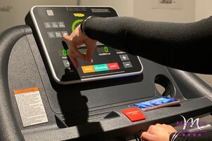 Una caminadora con pantalla digital, botón de parada de emergencia y un código QR.