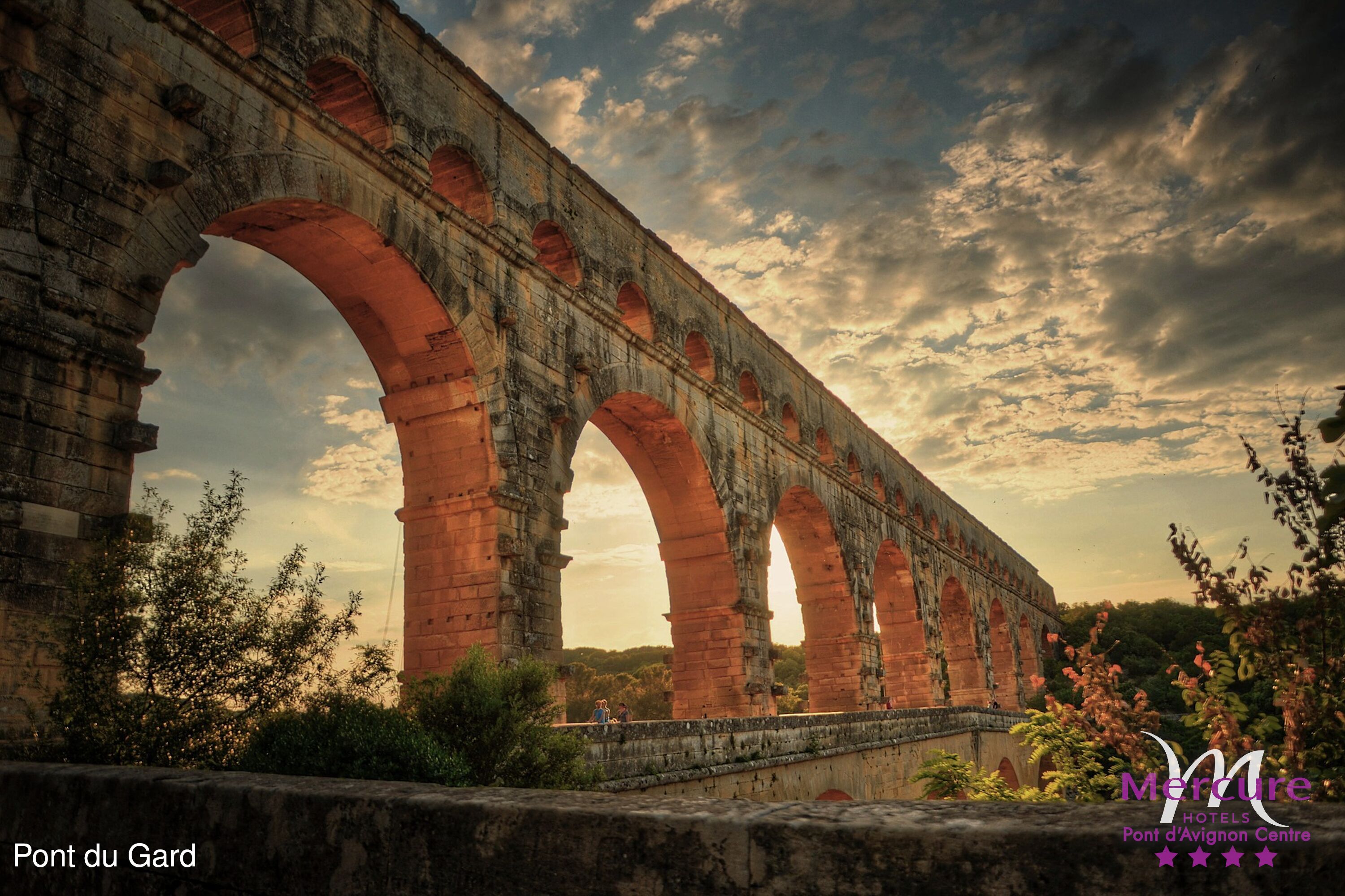 Pont du Gard, an ancient Roman aqueduct with multiple arches, set against a backdrop of a cloudy sky.