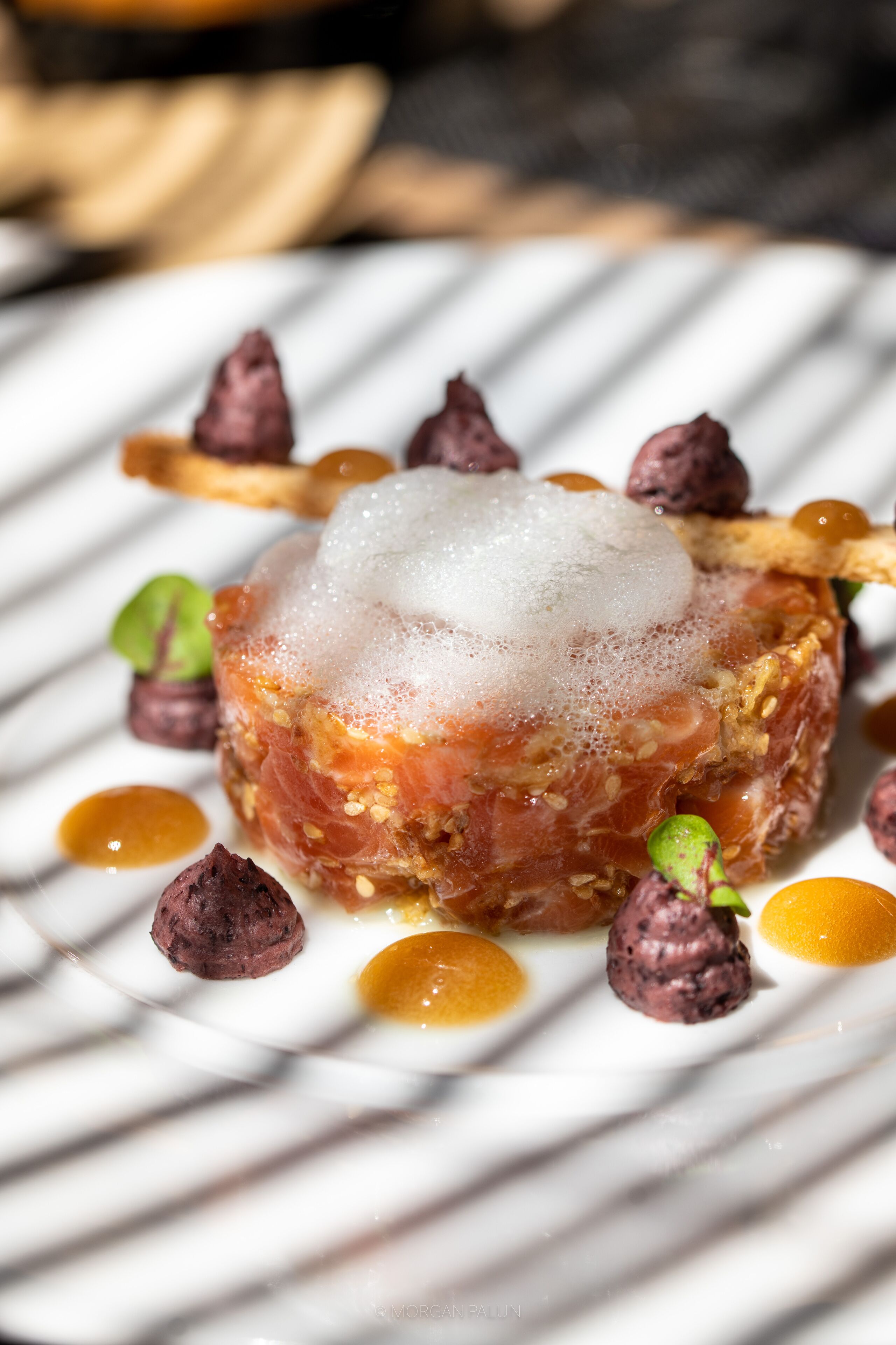 A dish with a spherical center, surrounded by various garnishes and sauces on a white plate.