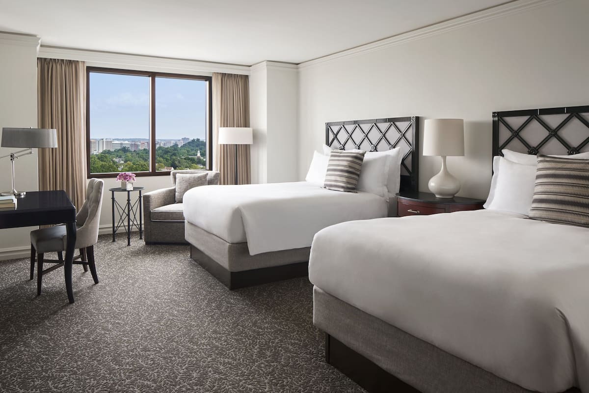 Habitación de hotel con dos camas, un escritorio, una silla y vista a la ciudad.