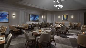 A spacious dining area with multiple tables and chairs, elegant lighting fixtures, and large abstract paintings on the walls.