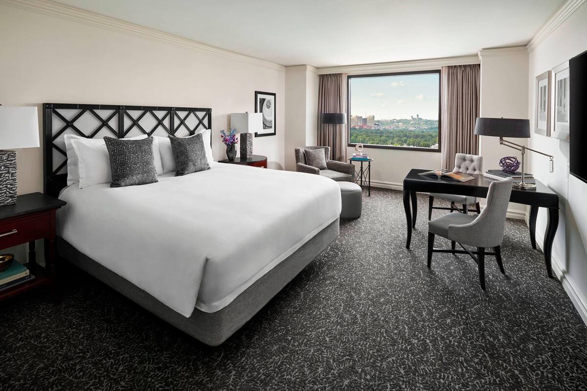 Habitación de hotel con una cama grande, un escritorio, una silla y vistas a la ciudad.