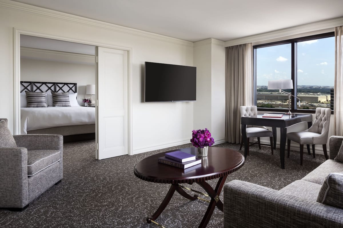 Habitación de hotel con cama, televisión, escritorio y sillas, y vista a la ciudad.