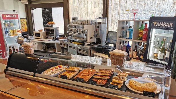 A bakery display case with various baked goods and a coffee machine in the background. - La Posada de El Chaflán (Madrid)