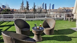 A rooftop terrace with wicker furniture and a table set for two, overlooking a cityscape. - La Posada de El Chaflán (Madrid)