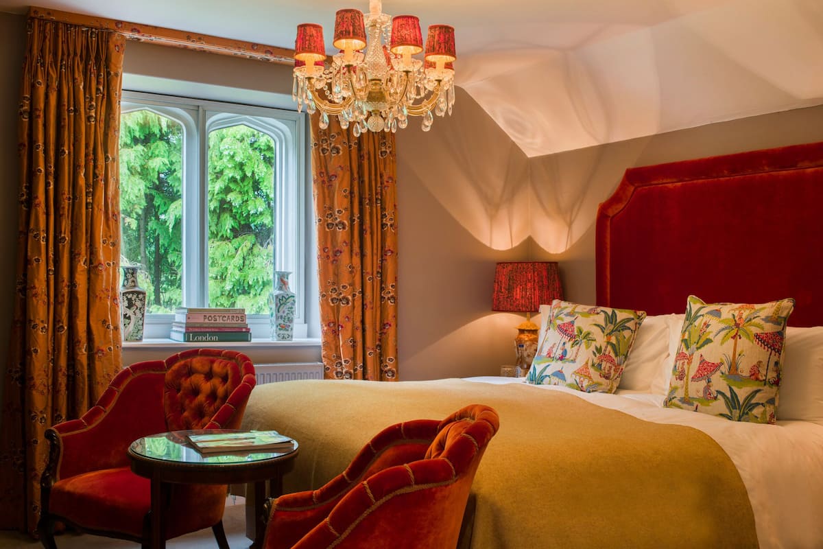 A hotel room with a large bed, a red upholstered chair, a small table, and a chandelier.