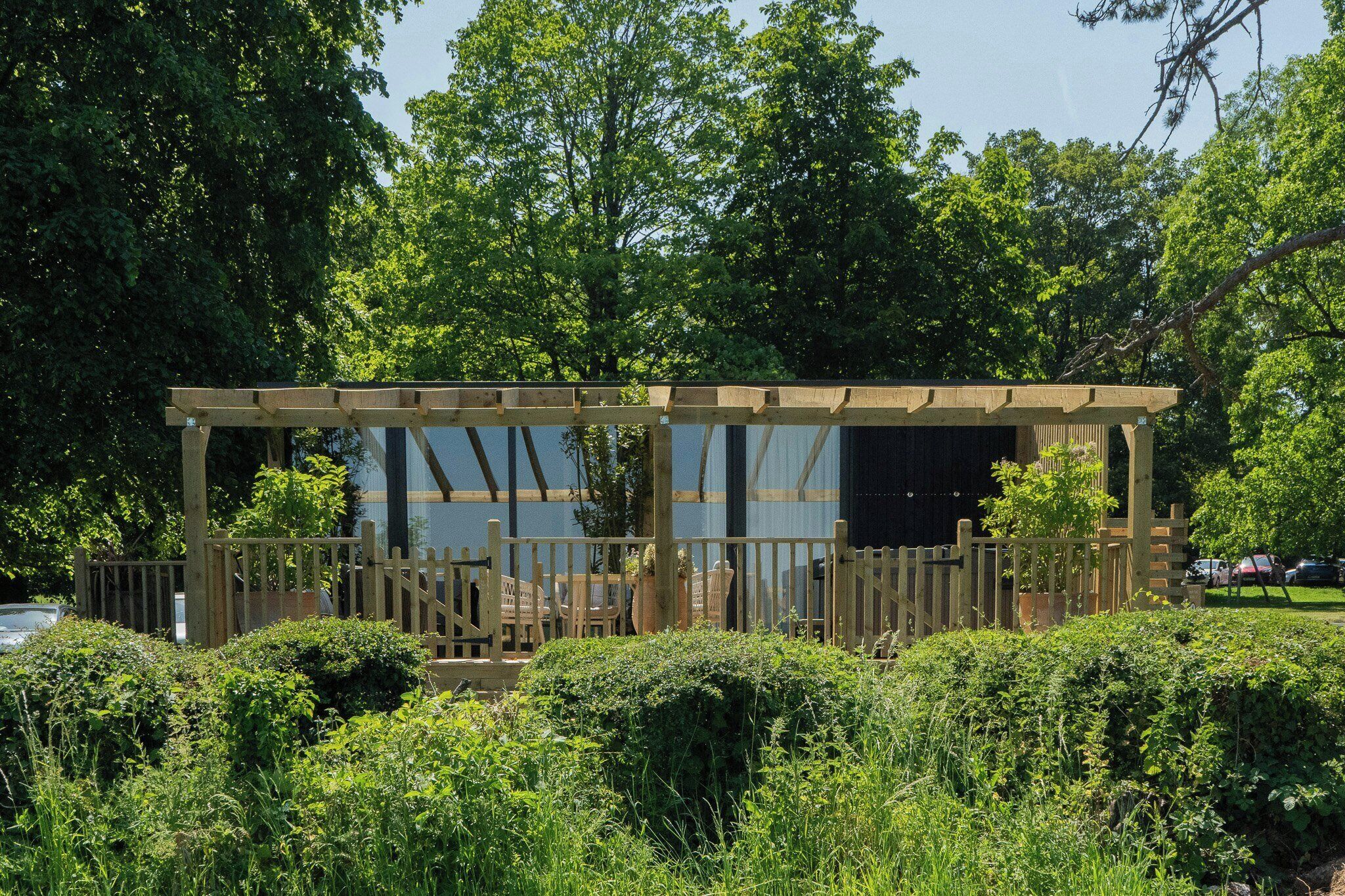A wooden pergola structure with seating, surrounded by lush greenery and trees.