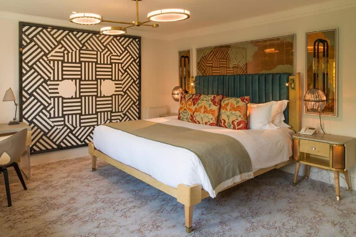 A modern hotel room with a large bed, a desk, and a patterned wall.