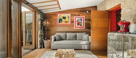 A modern living room with a grey sofa, wooden walls, and a glass door leading outside.