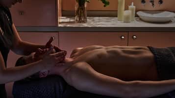 A massage therapy session in a room with a wooden cabinet, a vase with flowers, and candles on a table.