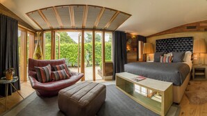 A modern hotel room with a curved ceiling, a large bed, a leather armchair, and a glass coffee table.