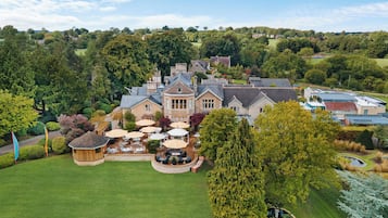 A large estate with a central building surrounded by a well-maintained lawn, outdoor seating area, and a pond.