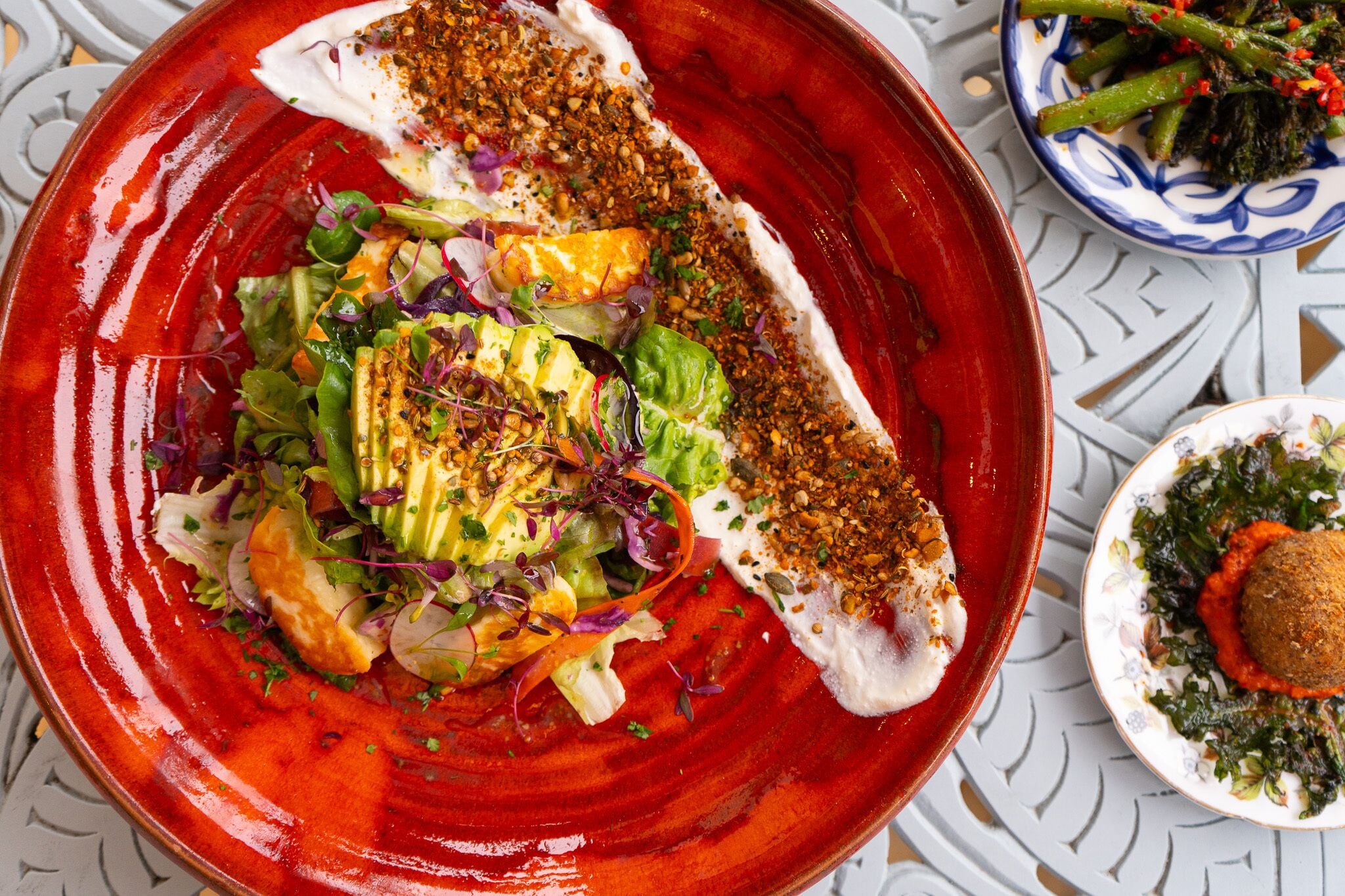 A red plate with a fish fillet, salad, and a side dish.
