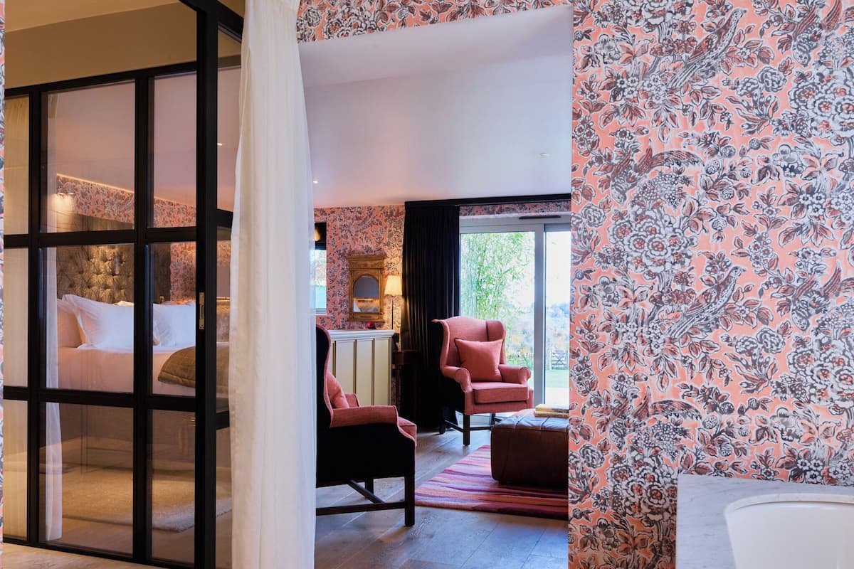 A hotel room with a bed, a chair, a small table, and a view of the outdoors.