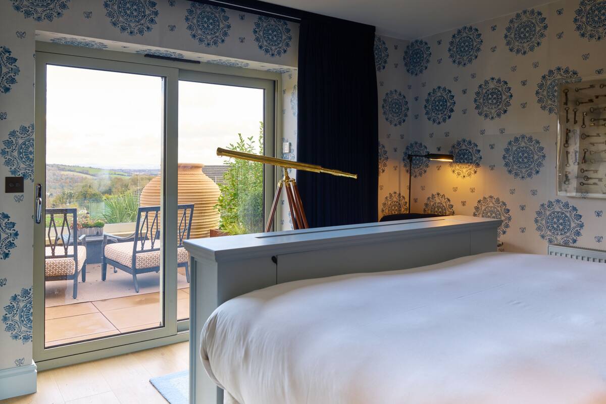 A bedroom with a large bed, a sliding glass door leading to an outdoor patio, and a telescope on a stand.