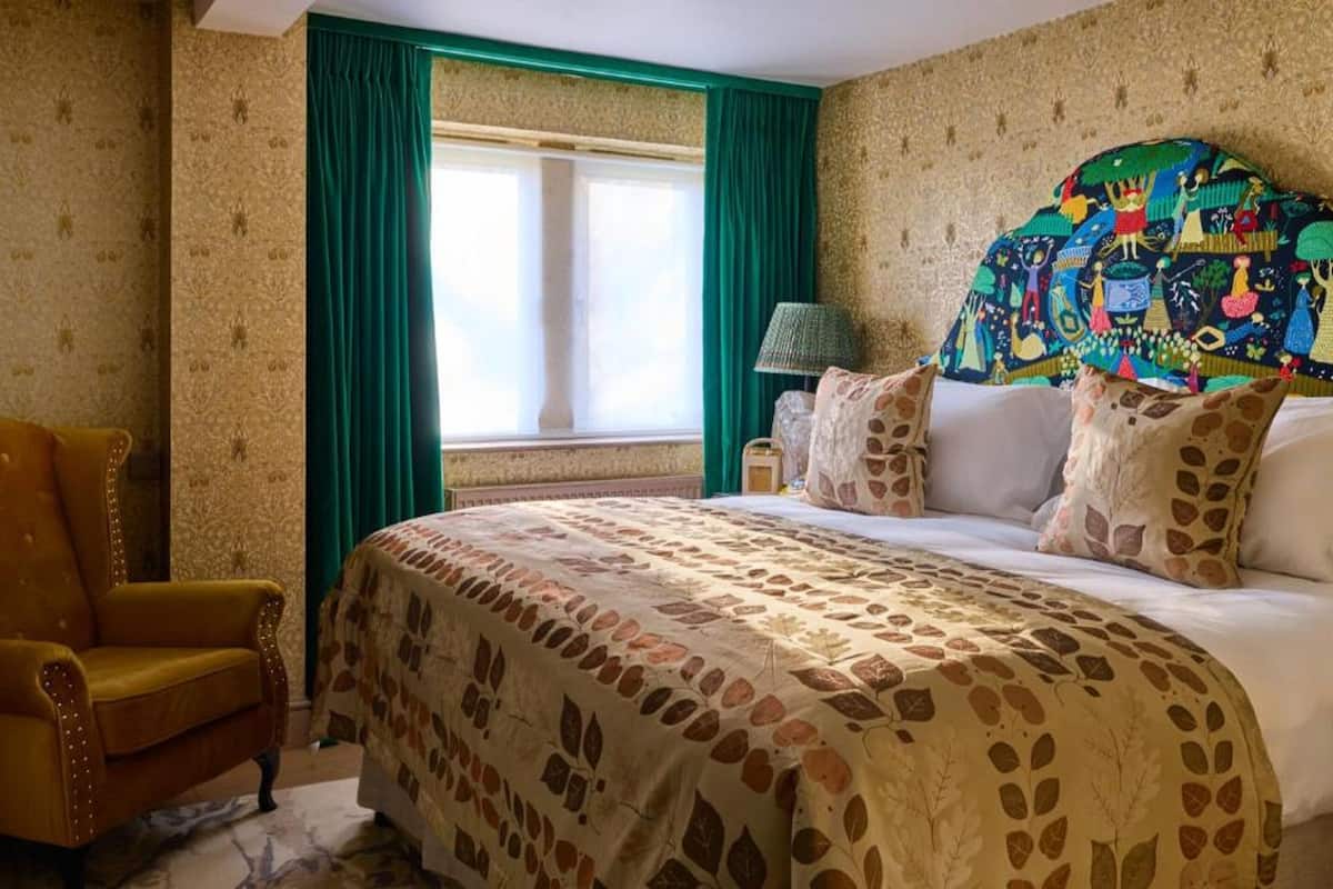 A bedroom with a large bed, green curtains, a patterned headboard, and a vintage armchair.