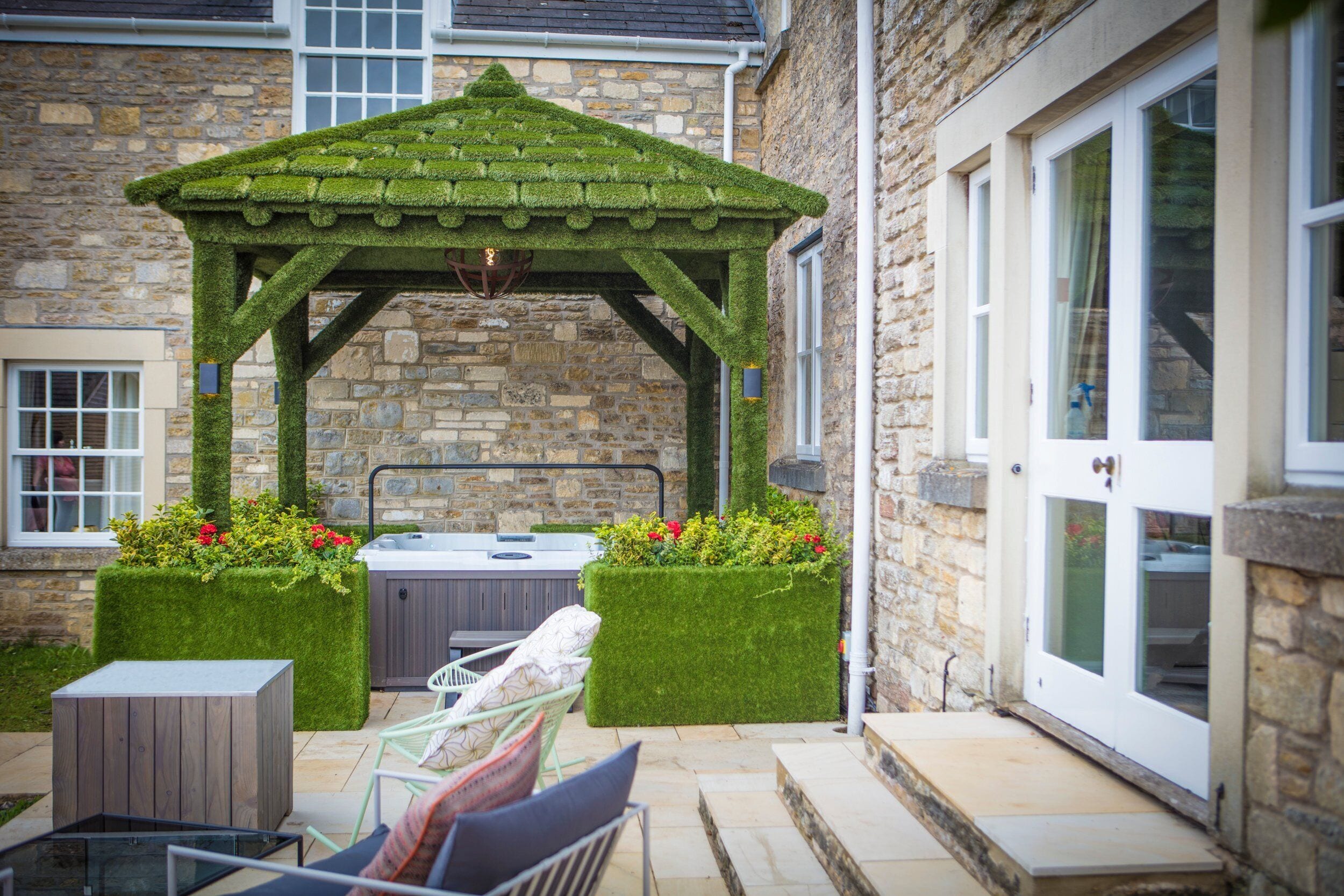 A stone building with a stone facade, a wooden deck, a hot tub, and a gazebo with a green roof.