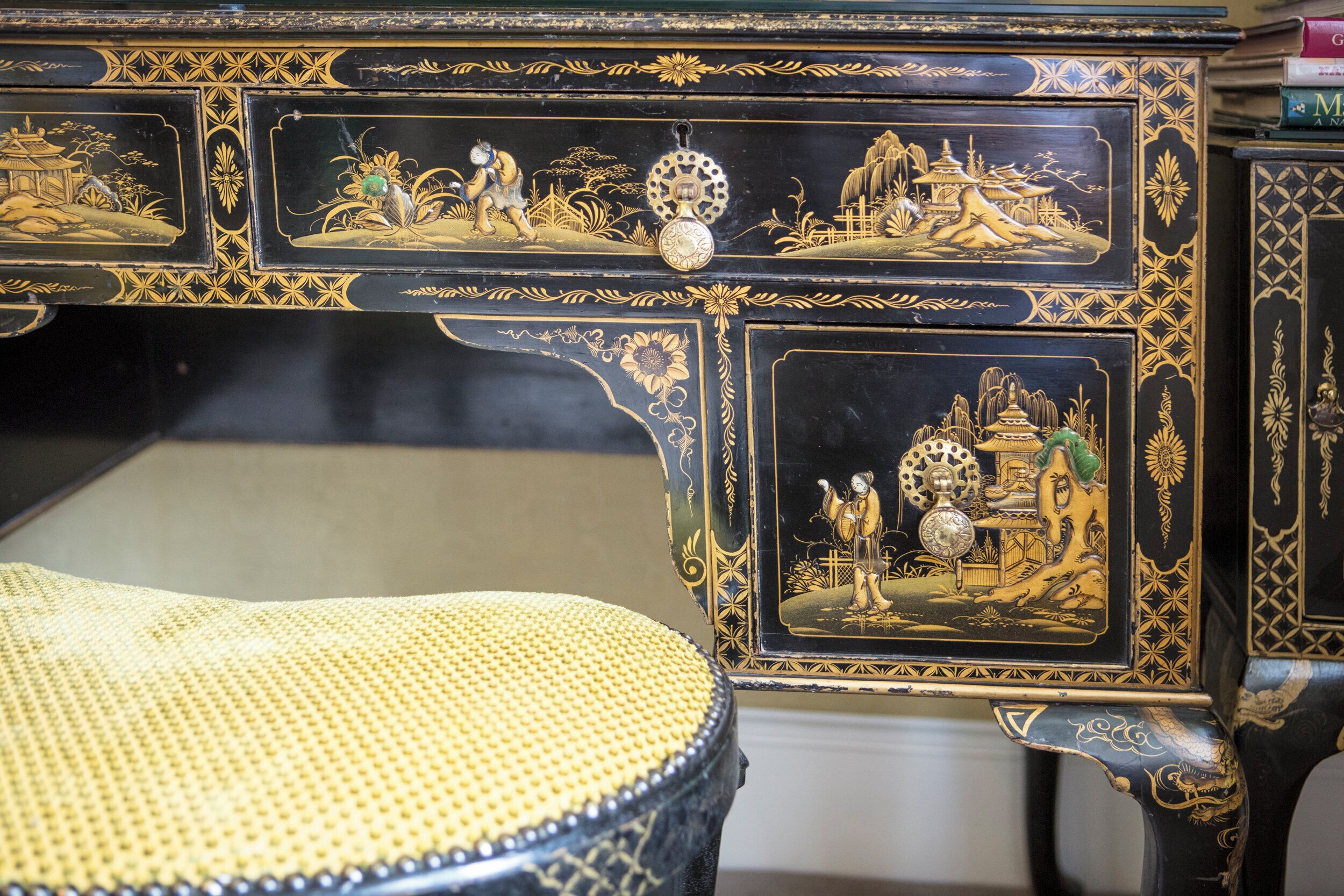 Une table noire et dorée, richement décorée de motifs complexes, accompagnée d’un tabouret en osier.