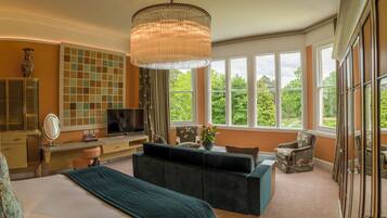 A bedroom with a large bed, a desk, a television, and a view of greenery through large windows.