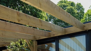 A hot tub under a wooden pergola with a view of a patio area.