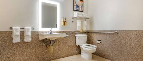 Un baño con lavabo, inodoro y barras de apoyo.