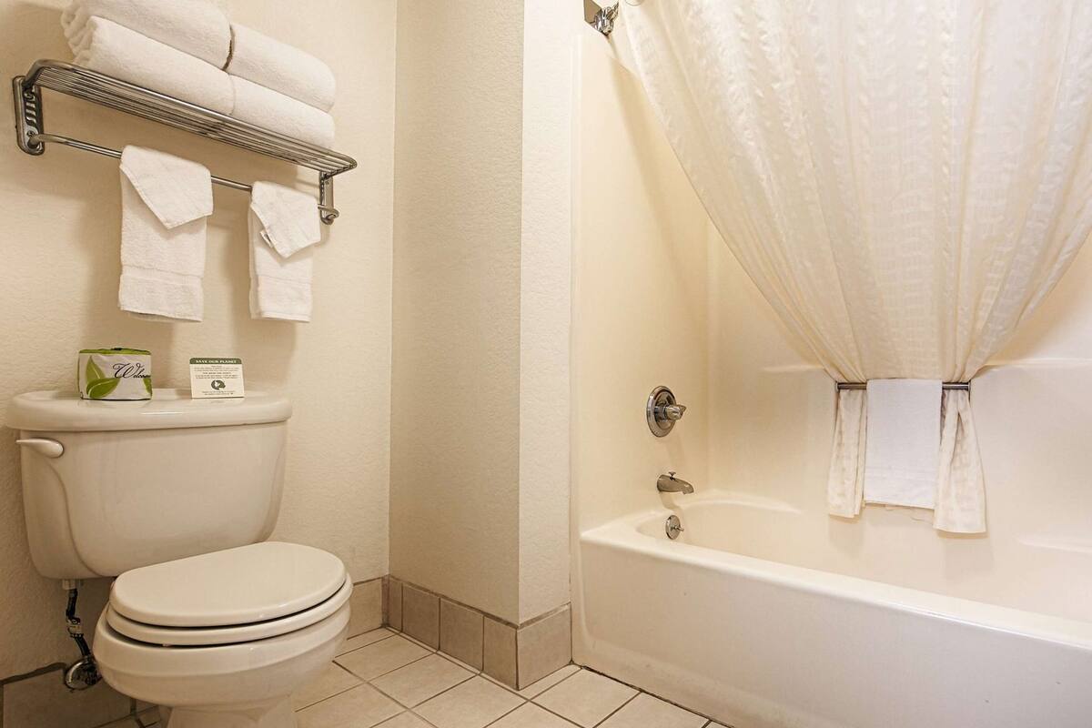 A bathroom with a toilet, a bathtub with a shower curtain, and a towel rack with folded towels.