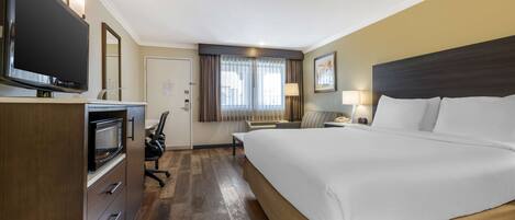 A hotel room with a large bed, a flat-screen TV, a desk with a lamp, and a chair.