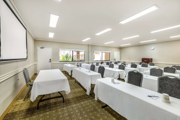 Un salón de conferencias con varias mesas, sillas y una pantalla de proyector.