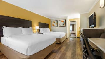 Ein Hotelzimmer mit zwei Betten, einem Fernseher, einem Schreibtisch und Bildern an der Wand.