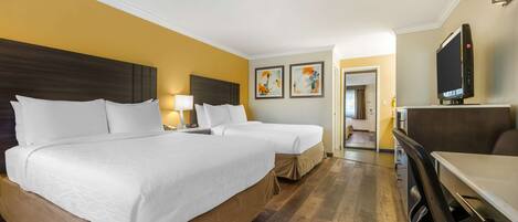 A hotel room with two beds, a TV, a desk, and artwork on the walls.