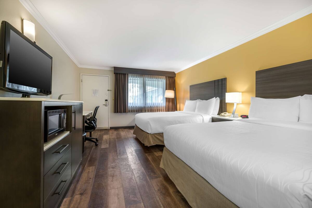 A hotel room with two beds, a desk with a computer, a television, and a window with curtains.