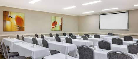 Un salón de conferencias con filas de mesas, sillas y una pantalla para proyector.