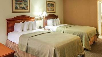 A hotel room with two beds, a nightstand, a lamp, and two framed paintings on the wall.
