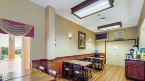 Comedor de hotel con mesas, sillas, un dispensador de agua y una kitchenette.