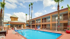 Una piscina con sillones de descanso, palmeras y un edificio de hotel con balcones.