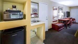 Una habitación de hotel con microondas, cafetera, lavamanos y un escritorio con silla.