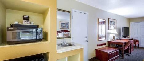 A hotel room with a microwave, coffee maker, sink, and a desk with a chair.