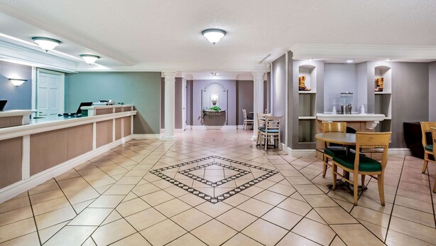 Un hall d’hôtel comprenant un comptoir d’accueil, un espace repas avec des chaises et une table en bois, et un sol au motif décoratif.