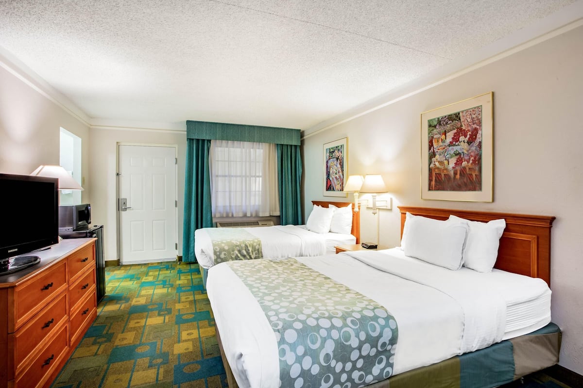 Une chambre d’hôtel avec deux lits, une télévision, une commode et un tableau au mur.