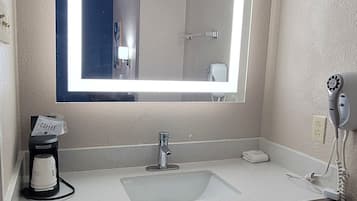 A bathroom with a large mirror, a sink, a coffee maker, and a hairdryer.