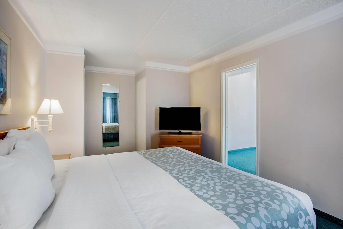 Une chambre d’hôtel avec un grand lit, un téléviseur à écran plat posé sur une commode en bois, une lampe et une vue sur l’océan par une porte coulissante.