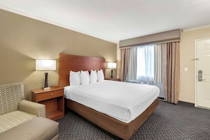 A hotel room with a large bed, two bedside tables, a nightstand, a sofa, and a window with curtains.