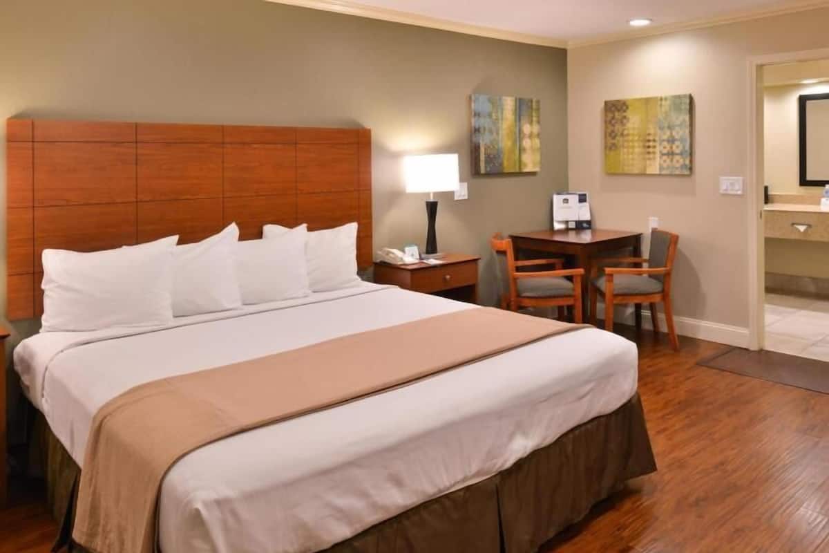 A hotel room with a large bed, a desk, a chair, and a small table.