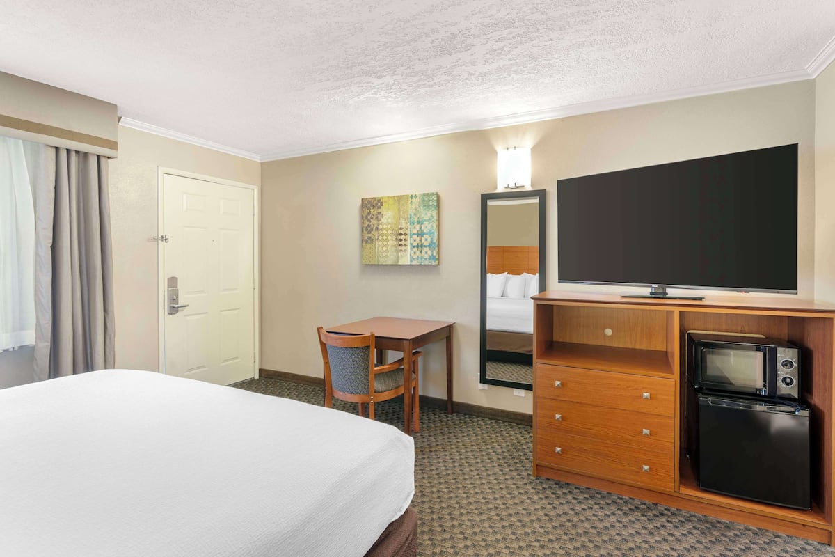 A hotel room with a bed, a desk, a television, a microwave, and a mirror.