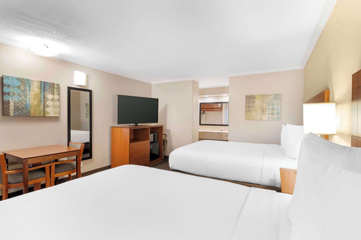 A hotel room with two beds, a desk, a television, and artwork on the walls.